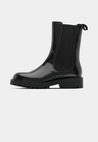 Fekete bokacsizma fényes felülettel, rugalmas oldalsó panelekkel, lekerekített orral és masszív, texturált talppal a jobb tapadás érdekében.