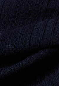 Navy blue dzianina z fakturowanymi wzorami ściągaczowymi. Włókna wydają się miękkie z wypukłymi elementami, z subtelnym połyskiem i głębią.