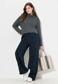 Marinblå vida byxor, randig polotröja i marinblått och vitt, samt vita sneakers. Har en mönstrad, randig tote-väska. Släta texturer.