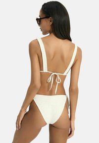 White bikini with wide straps, textured fabric, and a tied back closure. The bikini bottom features a low-rise cut and intricate stitching details.