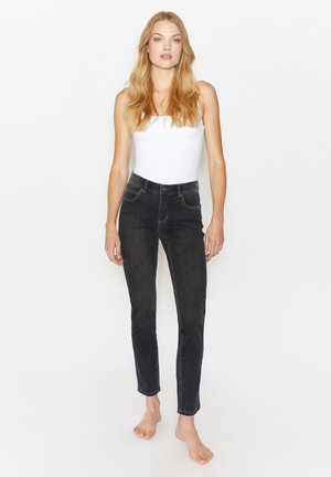 Zwarte high-waisted jeans met een slim fit, vijf zakken en contrasterende oranje stiksels. Draagt met een witte tanktop.