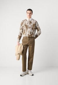 Brown and cream patterned sweater, beige bomber jacket, olive green trousers, and gray sneakers. Simple, contemporary design with varied textures.