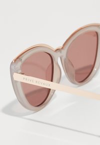 Óculos de sol com uma armação transparente de cinza claro, lentes com tonalidade rosa e um braço de metal com detalhes em rosa dourado, apresentando uma marca gravada.