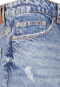 Jeans din denim cu un spălare albastră deschisă, cu nituri de cupru, pete estompate și un design clasic cu cinci buzunare.