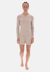 Beige pitkähihaiset yläosa ja siihen sopivat shortsit pehmeästä kankaasta. Yläosassa on pyöreä pääntie; shortseissa on resorivyötärö.