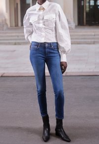 Vit långärmad skjorta med två bröstfickor, i kombination med blå smala jeans och svarta ankstövlar. Slät tyg och skräddarsydd passform.