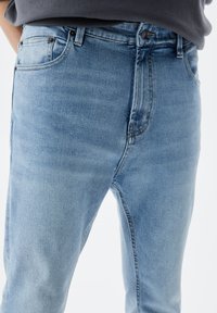Vaaleansiniset farkut slim fit -leikkauksella, joissa on viisi taskua, hienovarainen haalistuminen ja metalliset yksityiskohdat vyötäröllä ja taskuissa.