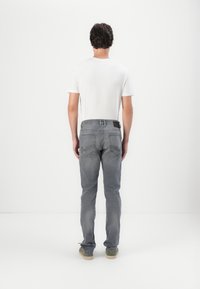 Szare jeansy z dżinsu o wąskim kroju, z tylną kieszenią i czarną metką na pasku. W zestawie z prostą białą koszulką.