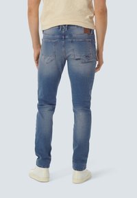 Blauwe denim jeans met een slim fit en lichte vervaging, voorzien van een bruine leren patch op de tailleband en twee achterzakken.