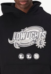 Sweatshirt preto com um grande logótipo bordado em cinza, decorado com espirais. Acentuado com três emblemas circulares que exibem as letras L, L, S.