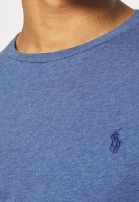 Blå bomulls T-shirt med klassisk rund halsringning, med en texturerad tyg och en liten broderad logga i mörkare blå.