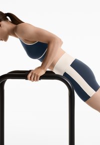Blå sportig crop top med vit kant, tillsammans med matchande högmidjade shorts med vit sidremsa, mot en enfärgad bakgrund.
