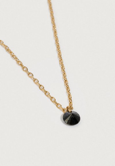 Zelta ķēdīte ar mazu, apaļu melnu fasētu piekariņu uz balta fona.