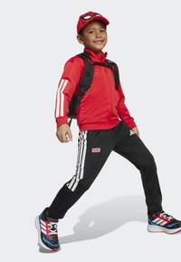 Rode zip-up jas met witte strepen, zwarte broek met witte strepen en "MARVEL" logo, rode Spider-Man pet, zwart-rode sneakers, zwarte rugzak.
