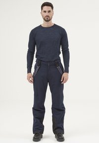 Navy ski pants with adjustable straps, made from durable material, and featuring reinforced black accents on the lower legs, paired with a navy long-sleeve shirt.
