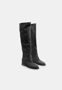 Botas negras por encima de la rodilla, hechas de suave ante, con un diseño ajustado y suelas planas. Textura lisa sin herrajes o patrones visibles.