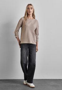 Top beige a maniche lunghe con strisce testurizzate, abbinato a jeans grigi scuri a gamba larga e scarpe bianche casual con suole marroni chiari.