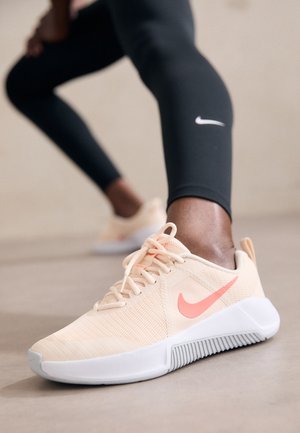 Person wearing black Nike leggings stretching, showing close-up of beige Nike sneaker with pink swoosh on a smooth floor.