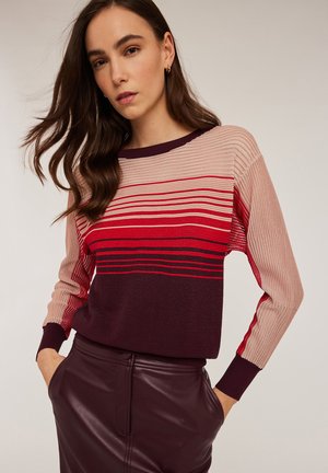 Pull en tricot avec des rayures horizontales dans des tons variés de rose, rouge et marron foncé. Texture côtelée ; coupe décontractée et manches longues.