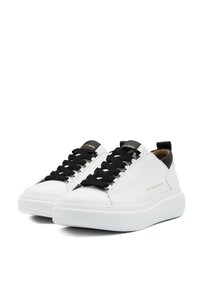 Sneakers in pelle bianca con lacci neri, dotate di una suola chunky bianca e un logo dorato di lato. Texture liscia, design minimalista.