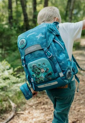 Sac à dos à motifs bleus avec un graphique marqué d'un personnage et de palmiers, comportant des zips et un badge circulaire sur le côté.