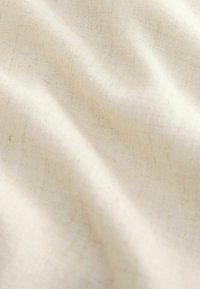 Lina audums krēmkrāsā ar smalku, teksturētu audumu, rādot maigas krokas un dabīgas šķiedras, radot mīkstu izskatu.
