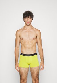 Boxer shorts de algodón amarillos con una cinturilla elástica negra que presenta el logo "BOSS". El diseño es ajustado, mostrando una textura suave.