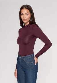 Bordowa body z długim rękawem, wykonana z elastycznego materiału, zestawiona z niebieskimi spodniami o wysokim stanie. Gładka faktura, dopasowany krój i okrągły dekolt.