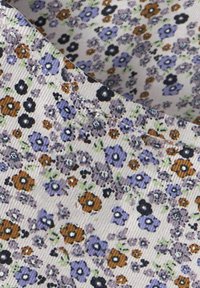 Kwiatowa tkanina na białym tle z drobnymi niebieskimi, fioletowymi i pomarańczowymi kwiatami. Charakterystyczna prążkowana faktura z rozproszonymi zielonymi akcentami.