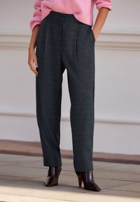 Grijze geruite broek met een getailleerd ontwerp, voorzien van plooien, zijzakken en een losse pasvorm, gecombineerd met donkere laarzen met hak.