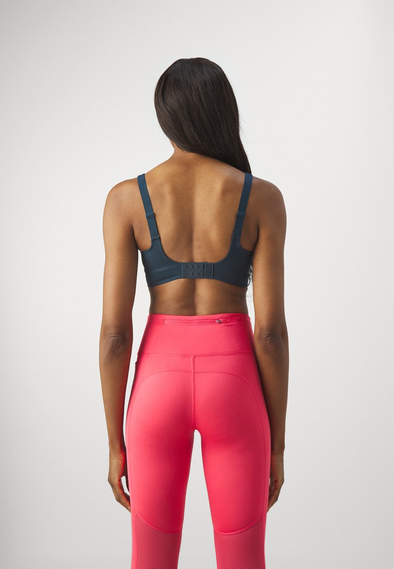 Sostén deportivo en azul oscuro con tirantes ajustables y cierre de gancho y ojal, combinado con leggings de alta cintura en rosa con paneles de malla.