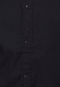 Černá košile s dlouhým rukávem s rozepínáním na knoflíky, vyrobená z texturované látky, se šesti černými knoflíky a vertikálními švy.