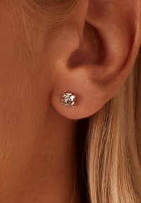 Boucles d'oreilles en pierres précieuses rondes et transparentes, montées en métal jaune. Vue rapprochée, mettant en valeur l'éclat et les détails de la pierre et du sertissage.