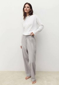 Biała bluzka z długim rękawem zestawiona z szarymi spodniami piżamowymi w paski, posiadającymi elastyczny pas i sznurek do ściągania. Miękka tkanina i luźny krój.