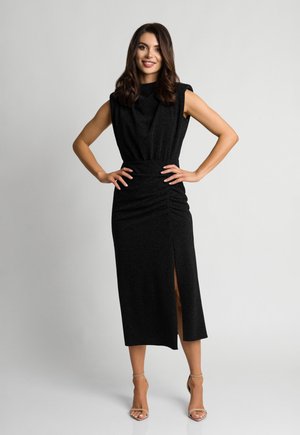 Czarna, bezrękawnikowa sukienka z wysokim dekoltem, z gathered w pasie i rozcięciem z przodu. Miękki, teksturowany materiał podkreśla kształt.