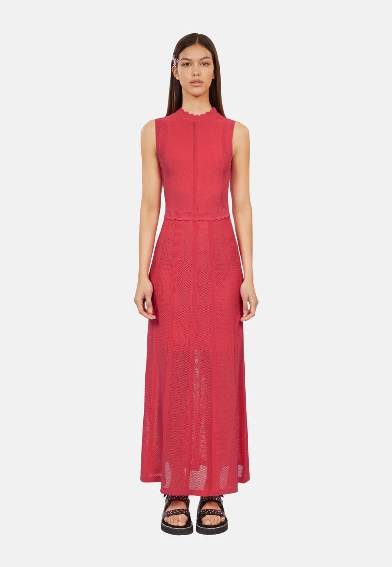 Robe maxi sans manches rouge avec un motif de tricot texturé, un col à volants et une taille cintrée. Associée à des sandales à plateforme noires.