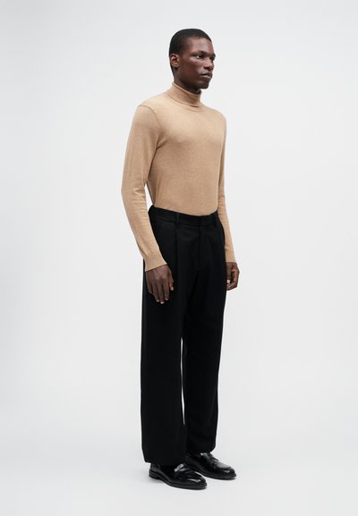 Suéter bege de gola alta combinado com calças pretas de cintura alta. O conjunto apresenta um ajuste slim e uma textura suave, complementado com mocassins pretos.