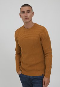 Sennepsgul strikkegenser med ribbestruktur, rund hals og lange ermer. Merkbar horisontal stripe over brystet.