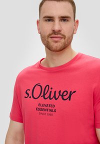 Roze t-shirt met korte mouwen, voorzien van een ronde hals en een zwarte opdruk met de tekst "s.Oliver Elevated Essentials Since 1969." Zachte stof.