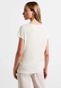 Lys kremfarvet kortærmet T-shirt med rund halsudskæring, glat tekstur og afslappet pasform. Sammen med lyse bukser.
