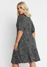 Musta mekko valkoisilla kukkakuoseilla, lyhyet hihat, istuva yläosa ja levenevä hame. Suora kangas, jossa on kevyt rakenne.