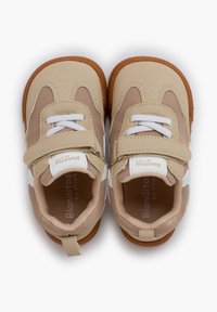 Zapatos de niño pequeños en color beige, con malla y ante, detalles en blanco, correa ajustable de Velcro, punta redondeada y suela de goma. Diseño bicolor con detalles de costura.