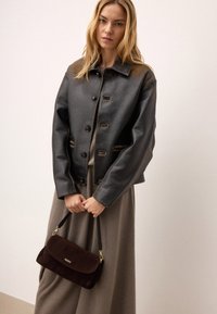 Czarna, błyszcząca skórzana kurtka z zapięciem na guziki i brązowymi akcentami. Połączona z brązową torebką z zamszu z złotym zapięciem.