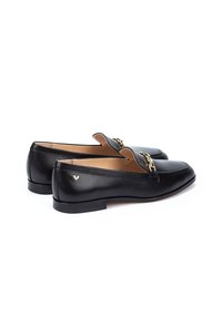 Mocasines de cuero negro con puntera redondeada, adornos de cadena en tono dorado y un pequeño logo en el tacón. Suela plana y diseño sencillo.