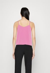 Camisola rosa con spalline sottili regolabili e vestibilità rilassata, abbinata a pantaloni neri a gamba larga. Tessuto morbido, design semplice e colori solidi.