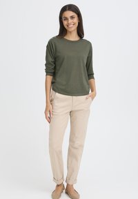 Pull en tricot vert olive avec manches trois quarts ; pantalon beige retroussé ; tissu doux ; design minimaliste ; sans motifs ni logos visibles.