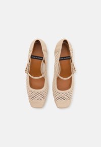 Chaussures Mary Jane beiges avec un dessus tissé, des accents en cuir lisse et un bout rond. Comprend une bride latérale avec une boucle et une semelle intérieure rembourrée.