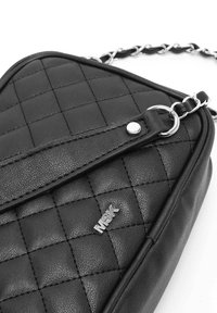 Borsa a tracolla in pelle trapuntata nera con design piatto, hardware argentato, tracolla a catena e dettagli del logo in rilievo. Motivo di superficie testurizzato.