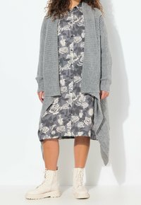 Šedý žebrovaný cardigan přes květinové šaty v šedé a bílé, doplněné krémovými bojovými botami. Výrazný vrstvený a otevřený přední střih.