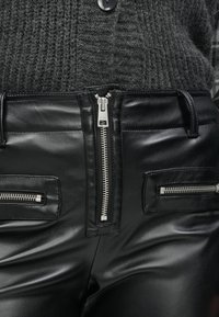 Μαύροι παντελόνια από ψεύτικο δέρμα με ψηλή μέση, κεντρικό φερμουάρ και δύο τσέπες με φερμουάρ, διακοσμημένα με ασημένιες μεταλλικές λεπτομέρειες. Μαλακή υφή.